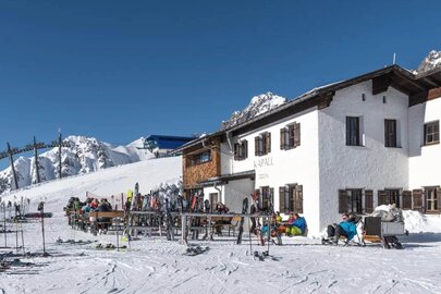 Ski house Kapall at 2330 m elevation with guests and skis in the snow.