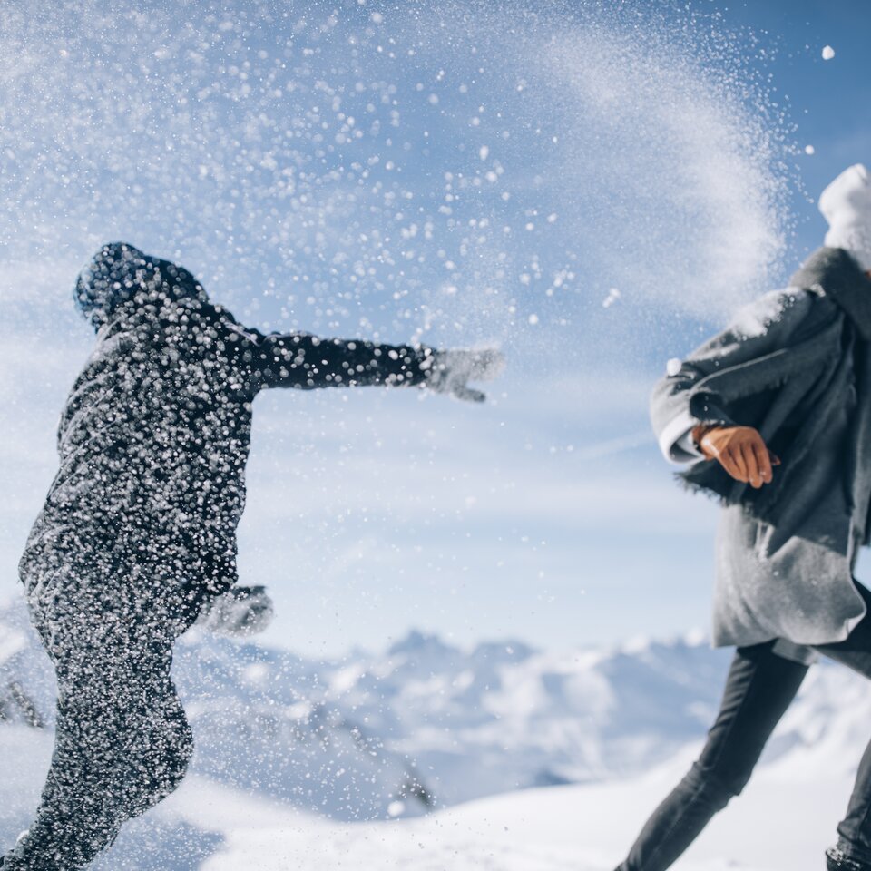 Two people having fun throwing snowballs in the mountain snow.