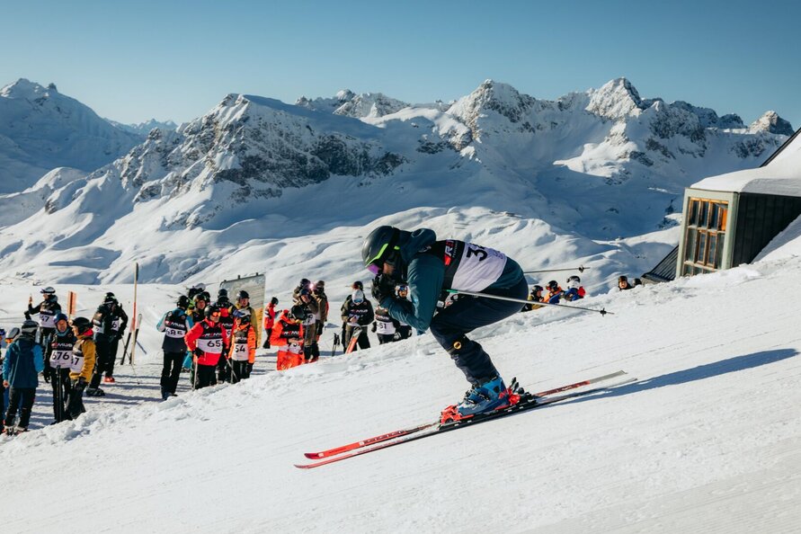 Skier starts at the White Ring race, spectators and snowy mountains in the background.