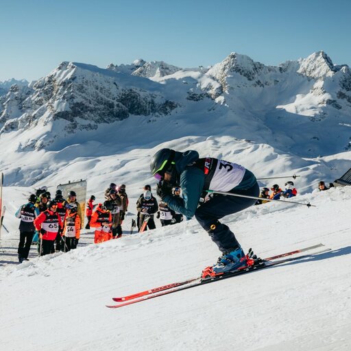 Ein Skifahrer startet eine Abfahrt, während Zuschauer auf der Seite stehen.