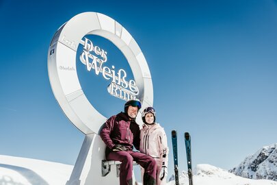 Zwei Personen posieren vor dem "Der Weiße Ring" Monument im Schnee.