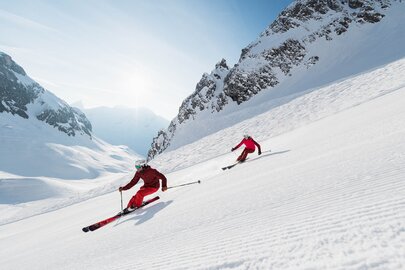 Zwei Skifahrer gleiten dynamisch den Schneehang hinunter.