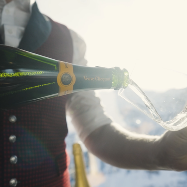 Person pouring champagne into a glass with mountain view.