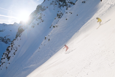 Two skiers on a snowy slope in sunlight.