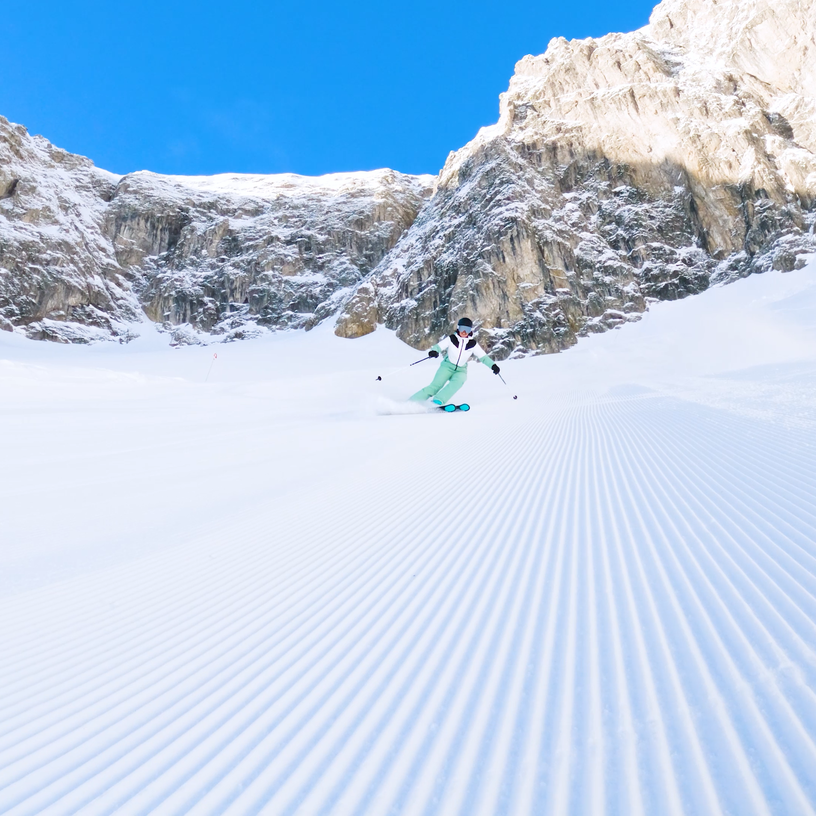 Skier on freshly groomed slope surrounded by mountains.