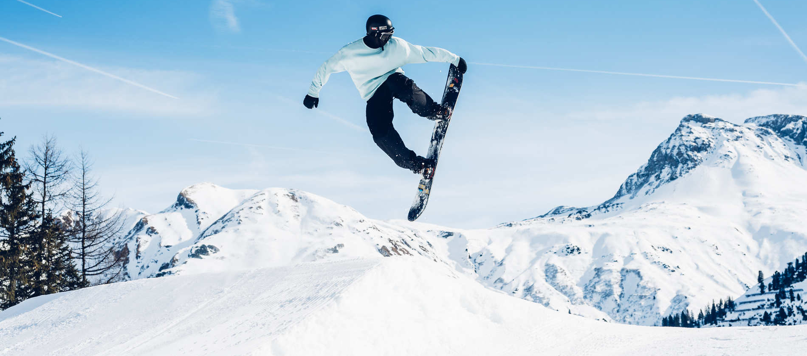 Person jumping with a snowboard against a backdrop of snowy mountains.