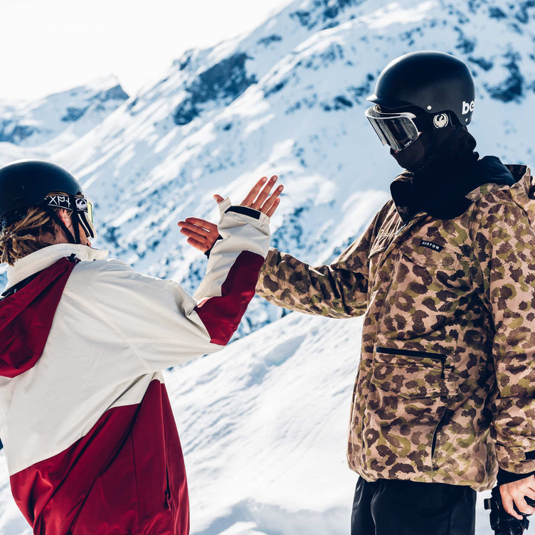 Two people in the snow giving a high-five in a mountainous winter landscape.