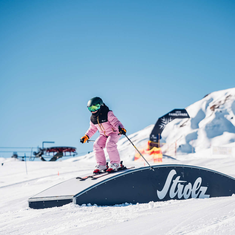 Child skiing over a ramp in the snow park.