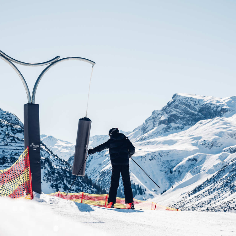 Person on skis at the lift station with snow-covered mountains in the background.