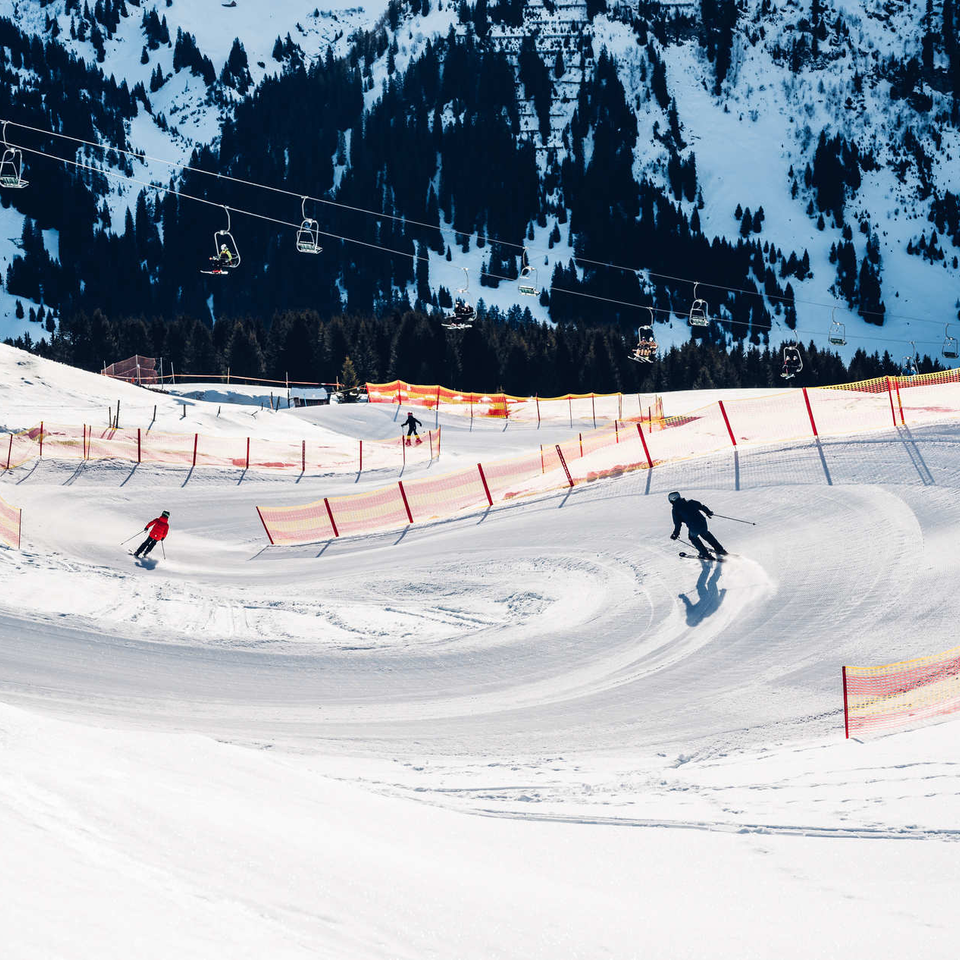 Skiers descend a winding, secured slope.