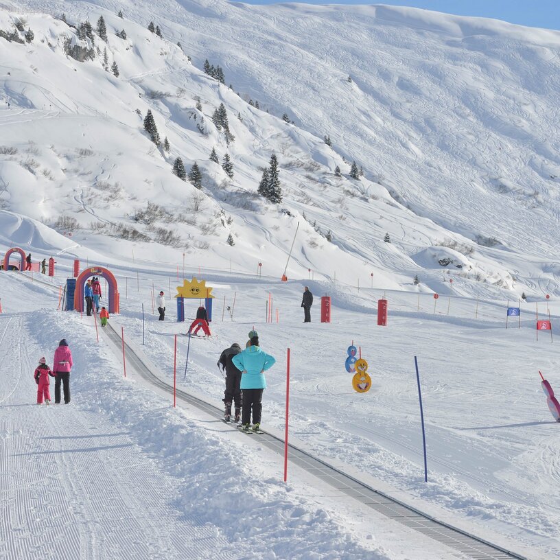 Families enjoying skiing and snowboarding on a beginner slope in the snow.