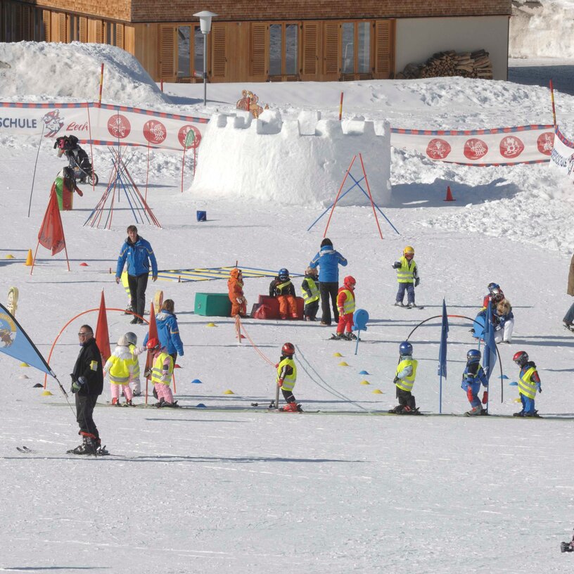 Children in a ski class with snow castle in the background.