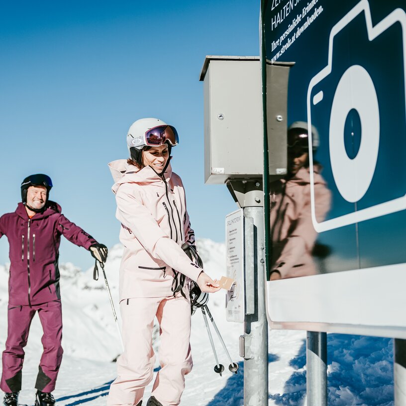 Two skiers take a photo at a photopoint in the snow.