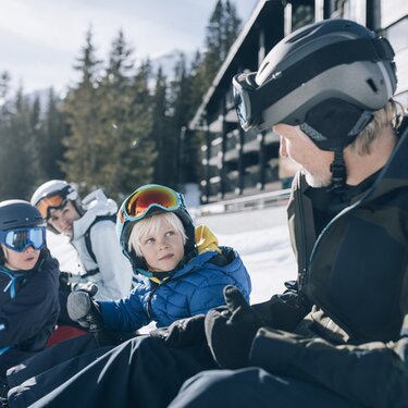 Family sitting in ski gear in the snow having a conversation.