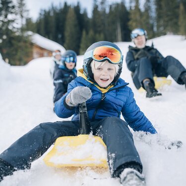 Children and adults sledging and laughing in the snow.