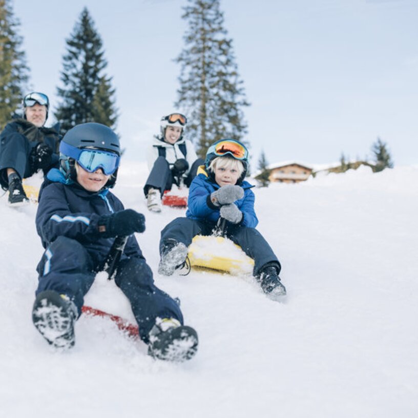 Children sledging in the snow, wearing ski helmets and goggles.