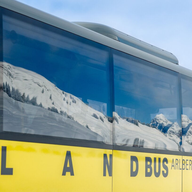 A yellow bus and snow-covered Alps reflected in the windows.