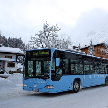 A blue bus driving on a snowy road in the Alps.