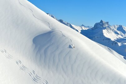Skier leaves curvy trail on a snow-covered slope.
