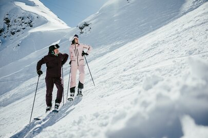 Zwei Skifahrer, ein Mann und eine Frau, auf einer verschneiten Skipiste.