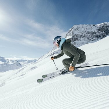 Skier skiing down a sunny, snow-covered mountain slope.