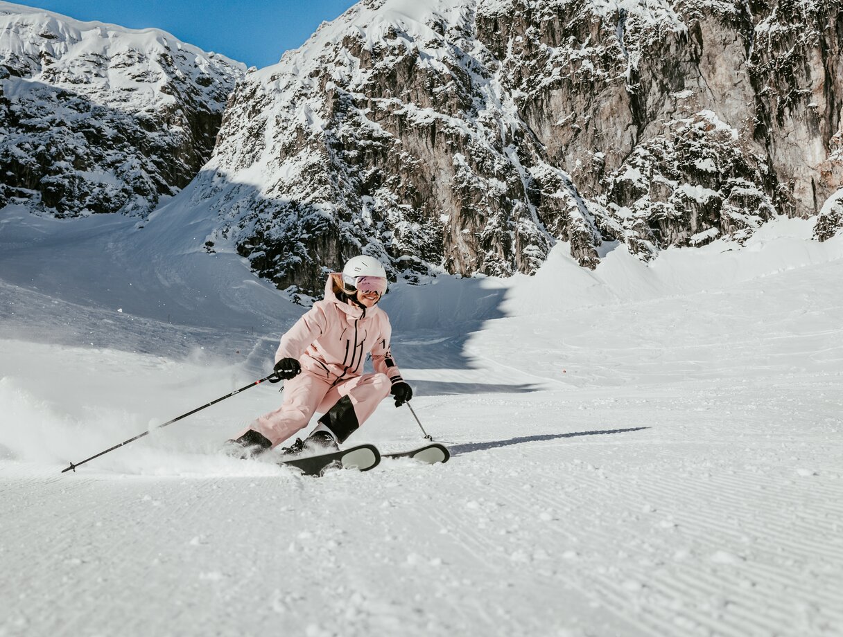 Skifahrerin in rosa Anzug bei sonnigem Wetter in den Bergen.