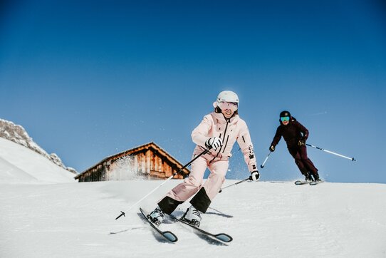 Zwei Personen fahren bei strahlend blauem Himmel Ski.