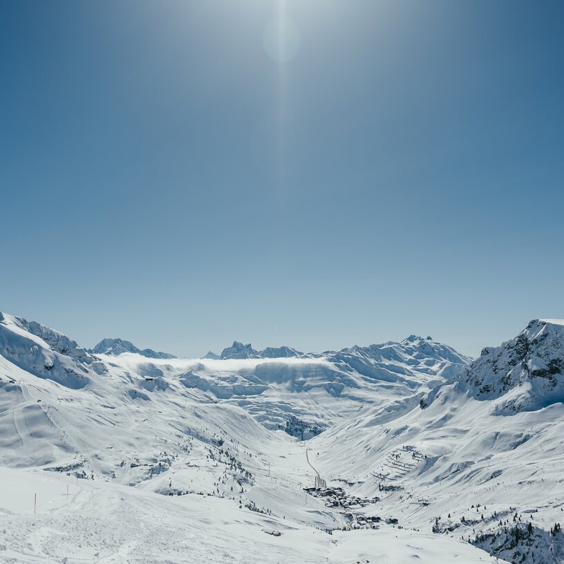 Verschneite Berge und Tal bei strahlendem Sonnenschein in der Skiregion Lech Zürs.