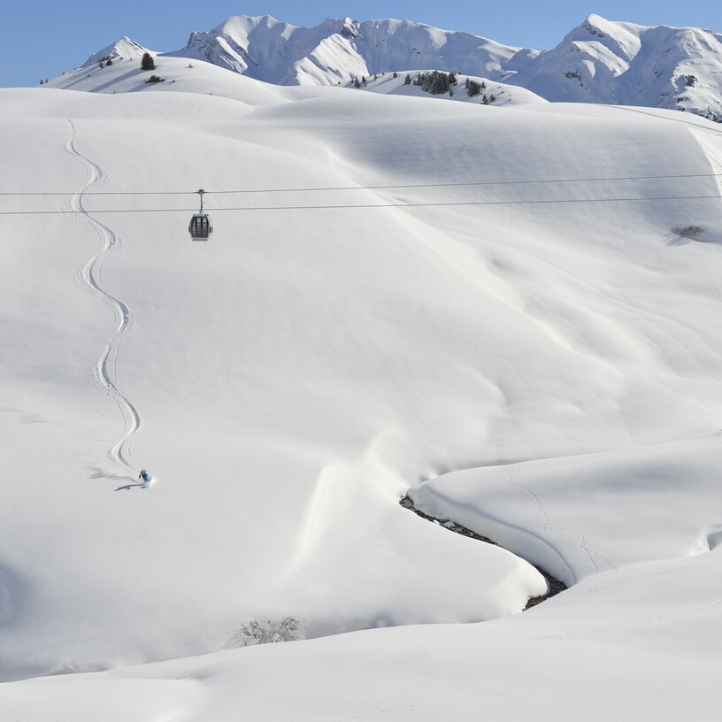 Eine verschneite Landschaft mit einer Seilbahn und Skifahrerspuren in der Skiregion Lech Zürs.