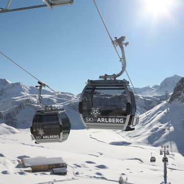 Seilbahn mit Logo von "Skiregion Lech Zürs" vor verschneitem Bergpanorama.