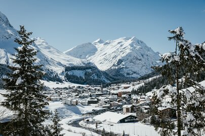 View of a snow-covered village in the Alps, surrounded by high mountains and fir trees in Lech Zürs ski resort.