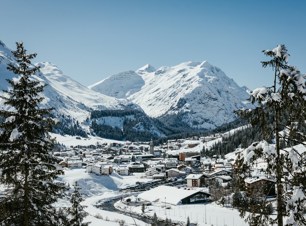 View of a snow-covered village in the Alps, surrounded by high mountains and fir trees in Lech Zürs ski resort.