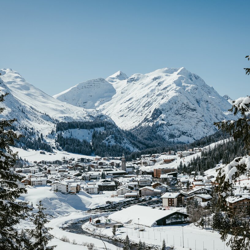View of a snow-covered village in the Alps, surrounded by high mountains and fir trees in Lech Zürs ski resort.