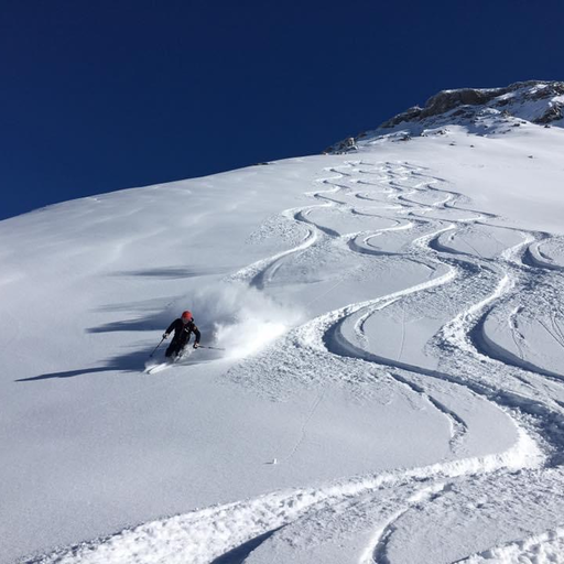A skier carves elegant turns in fresh powder snow on a steep slope under a clear blue sky.