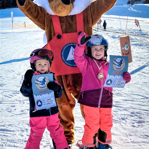 Two children in ski gear with mascot on the slope.