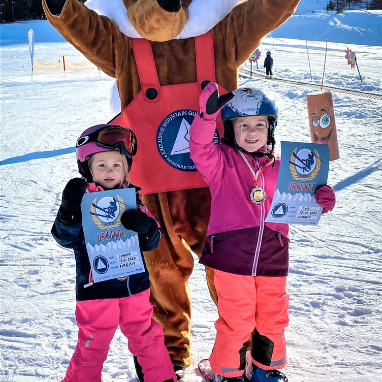 Two children in ski gear with mascot on the slope.