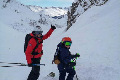 Two skiers in mountainous terrain, ready to descend.