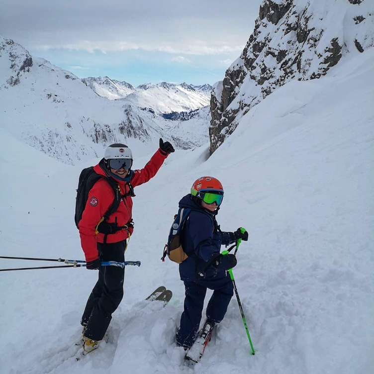 Skilehrer mit jungem Skischüler im Berggelände, bereit für die Abfahrt.
