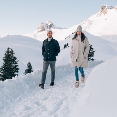 Paar spaziert im Schnee durch eine verschneite Landschaft.