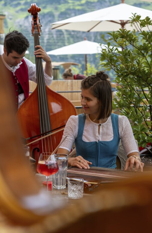 Frau in traditioneller Kleidung spielt Zither, daneben steht ein Bassist.