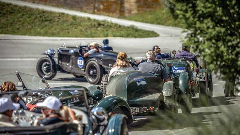 Several vintage cars on a road. Drivers and passengers enjoying the open-air ride.