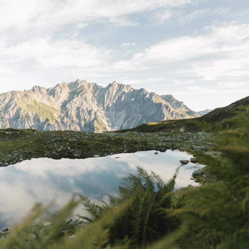 A small mountain lake reflects rocky peaks under a clear sky.