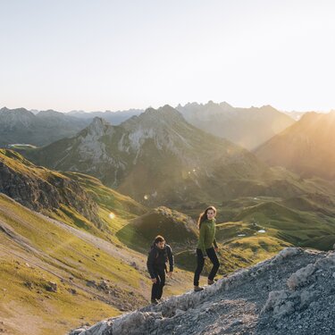 Two people hiking in mountainous terrain at sunrise.
