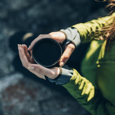 Person hält eine warme Tasse auf einer felsigen Oberfläche.