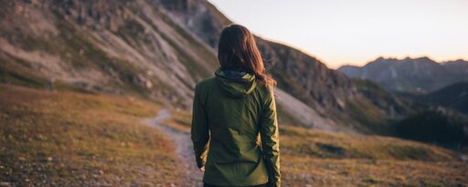 Woman in green jacket hiking in the mountains at sunset.
