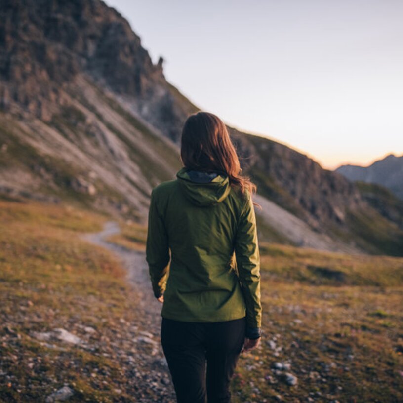 Frau in grüner Jacke wandernd bei Sonnenaufgang in den Bergen.