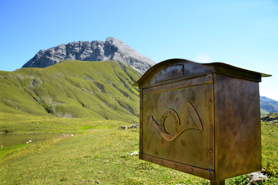 An old mailbox on a meadow with a mountain backdrop. 