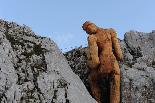 Large wooden sculpture of a man in a rocky mountain landscape.