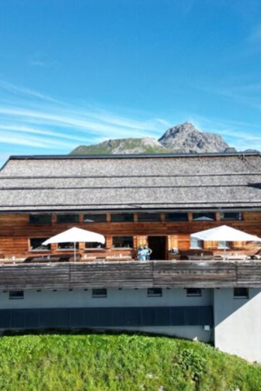 A mountain lodge at Kriegerhorn family mountain with a terrace and umbrellas against an alpine backdrop.