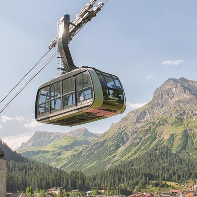A cable car travels over a valley towards the Kriegerhorn family mountain, with scenic mountains in the background.